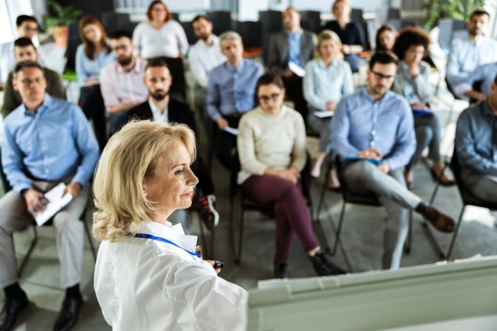 Senior female doctor giving presentation to group of people in board room.